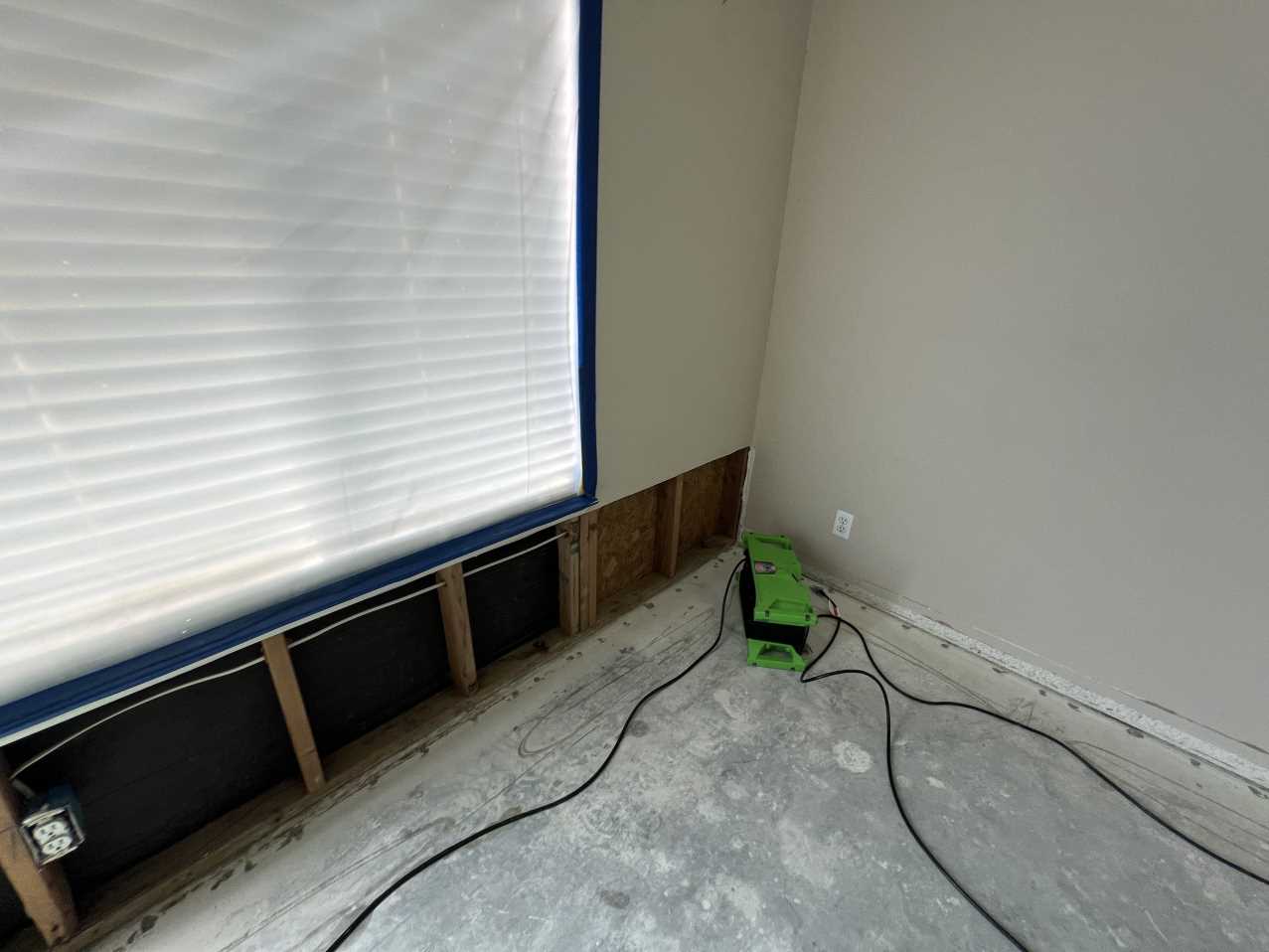 Water mitigation in progress showing the lower section of a wall opened for structural drying, with air movers addressing hidden water damage and preventing mold growth during bedroom restoration.