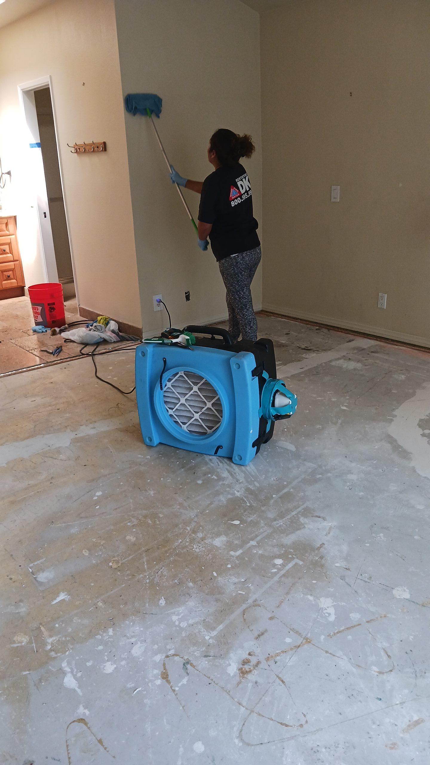 Technician performing soot removal on walls while using professional structural drying equipment (air mover) for combined fire and water damage cleanup and property restoration.
