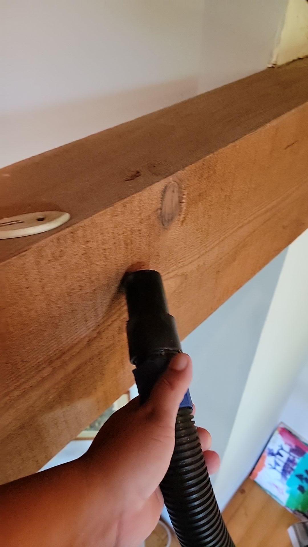 Technician performing soot vacuuming and initial cleanup on an exposed wooden beam, a crucial step in emergency fire damage mitigation and preparing the structural elements for full smoke removal and property restoration.