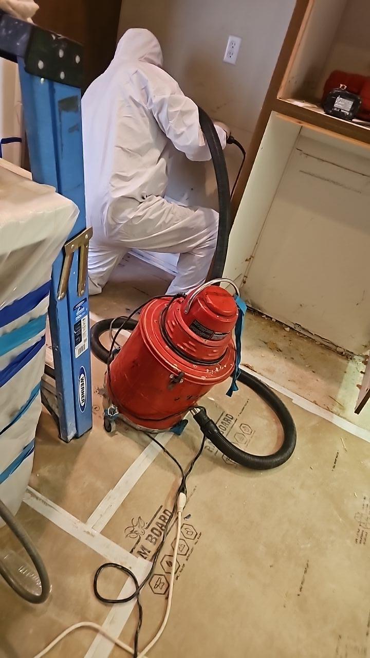 A technician in a protective suit uses a professional extractor to perform water damage cleanup. Our team uses specialized equipment to remove debris and moisture, a critical step in our water mitigation process to restore the property after a leak.