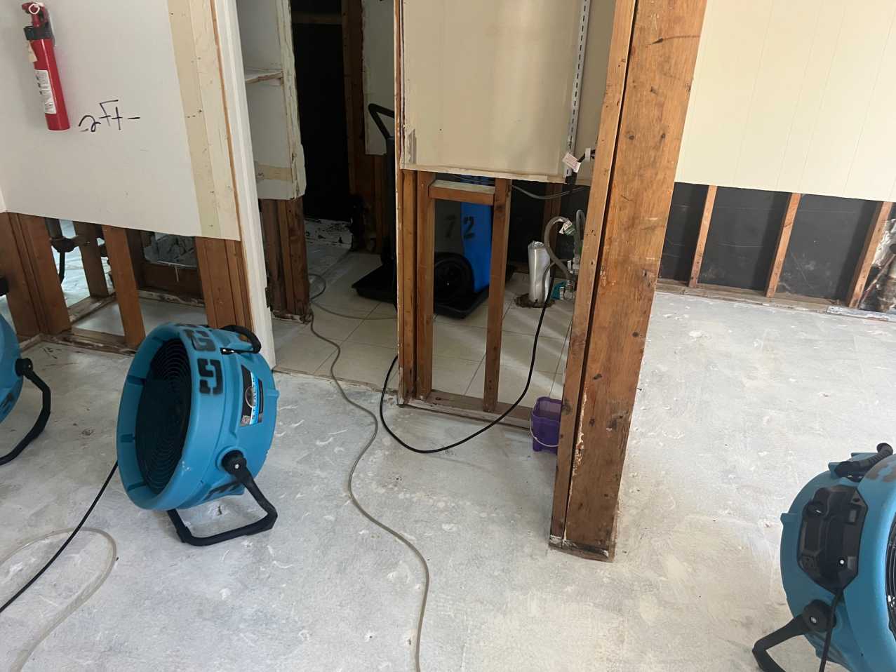 Reconstruction in progress showing removed drywall and vinyl plank flooring in a hallway, with air movers performing structural drying after mitigation and preparing the area for property restoration and rebuild.