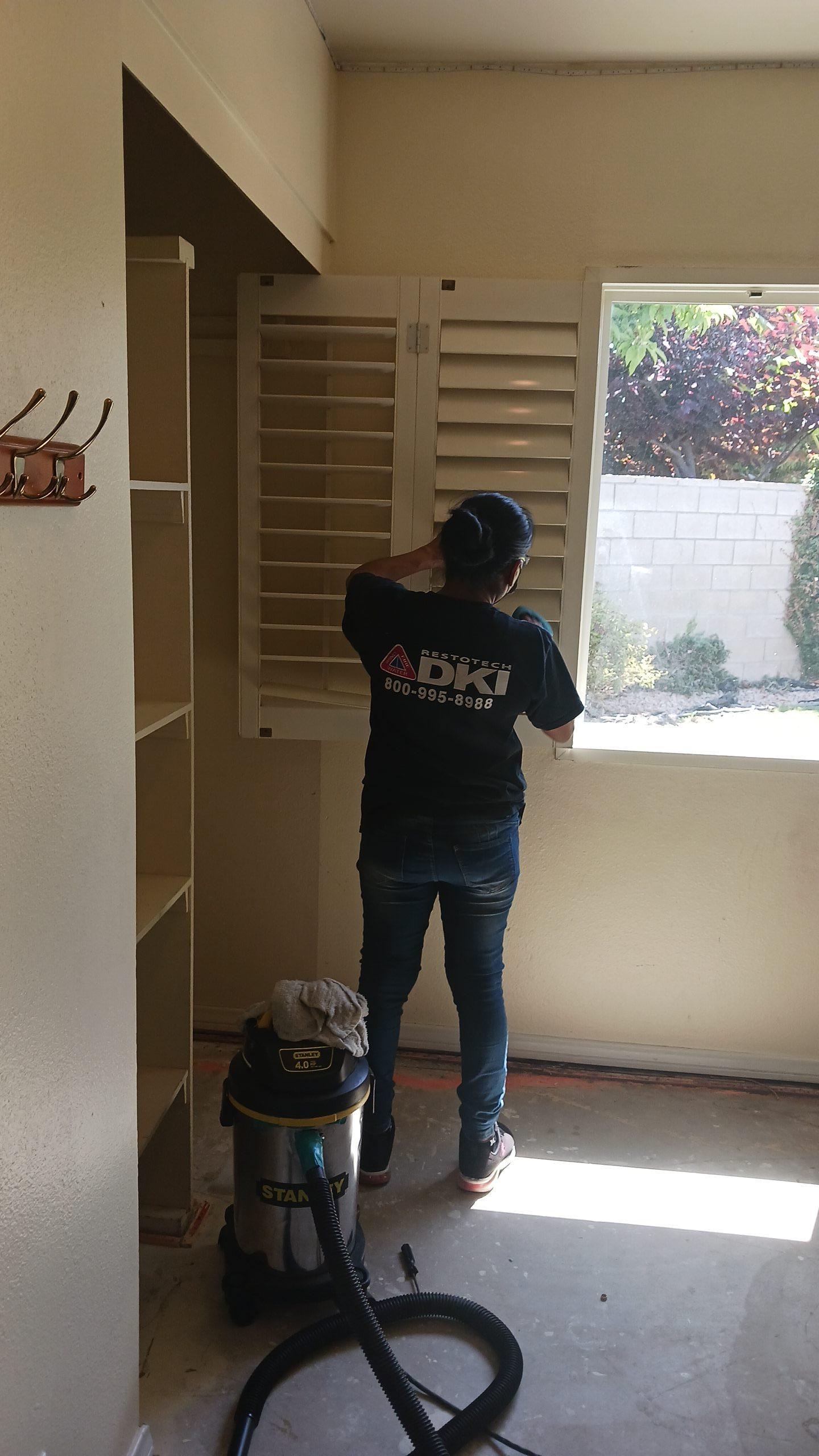 Detailed fire damage cleanup in a bedroom, where a technician is performing soot and smoke residue removal from shutters and windows as part of comprehensive property restoration services.
