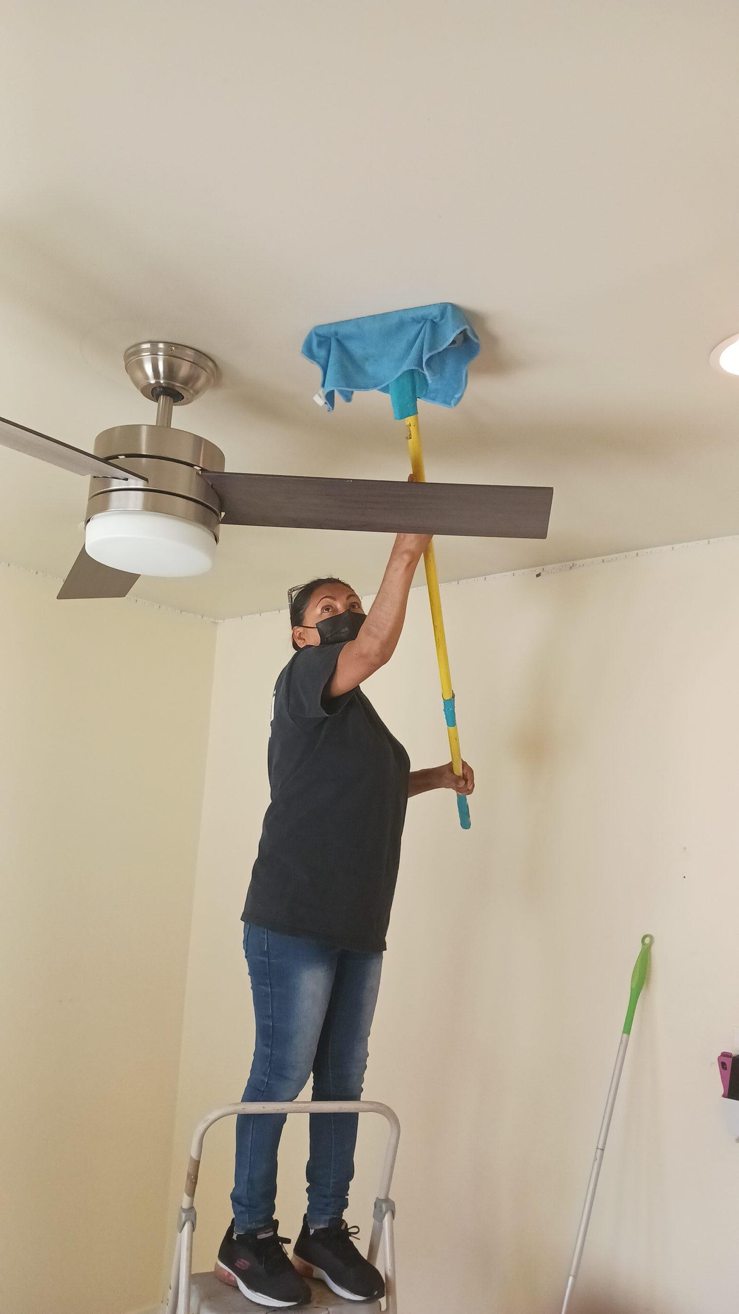 Technician performing detailed smoke and soot removal from ceiling fan and surfaces, vital step in fire damage cleanup and complete property deodorization and restoration after an incident.