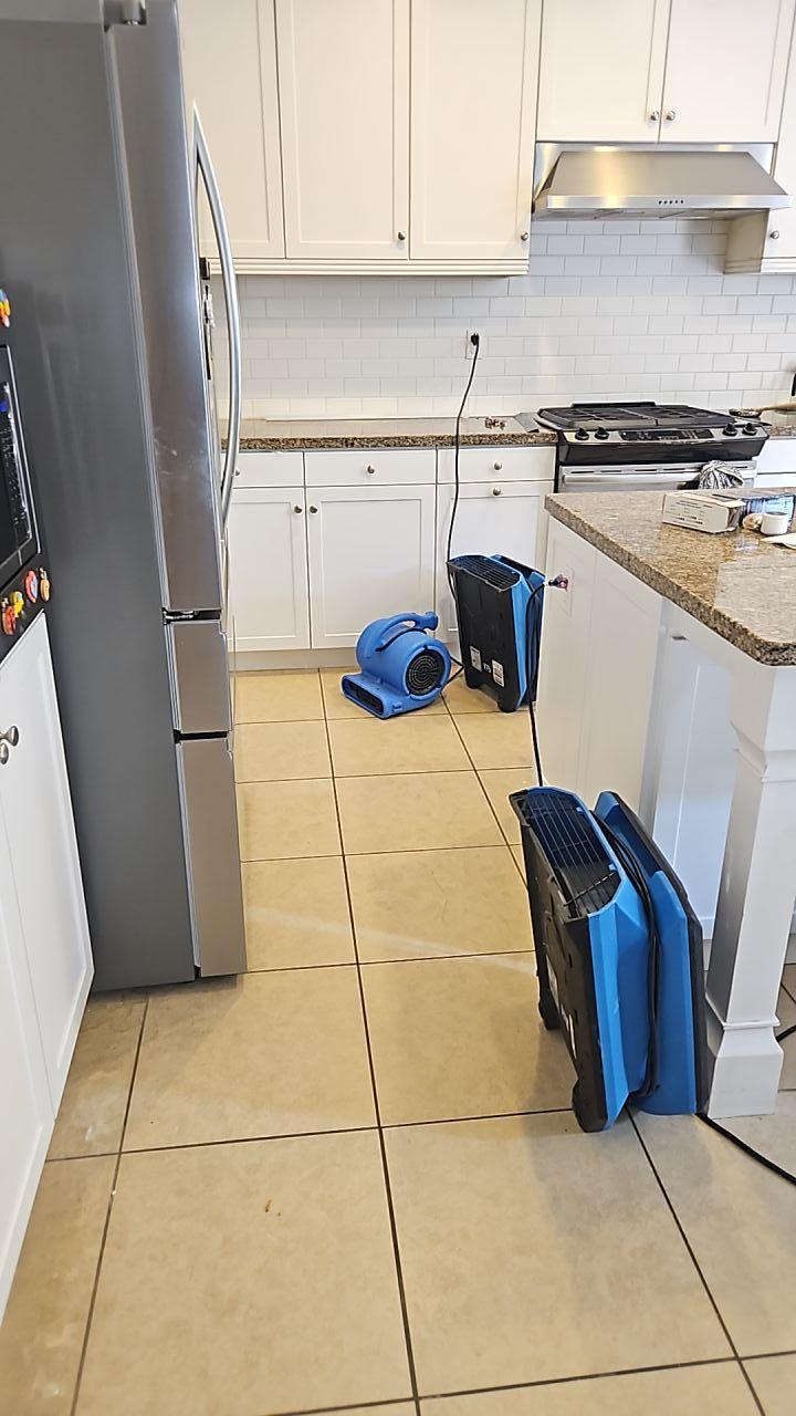 Water mitigation in progress showing air movers and fans set up on a tile floor for focused structural drying and dehumidification, critical for complete kitchen restoration after water damage from a plumbing leak.