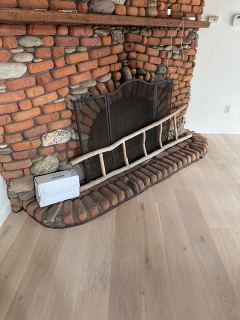 Final restoration of the living area after smoke damage, showcasing newly cleaned brick/stone fireplace and newly installed hardwood flooring, with complete soot cleanup and odor removal services.