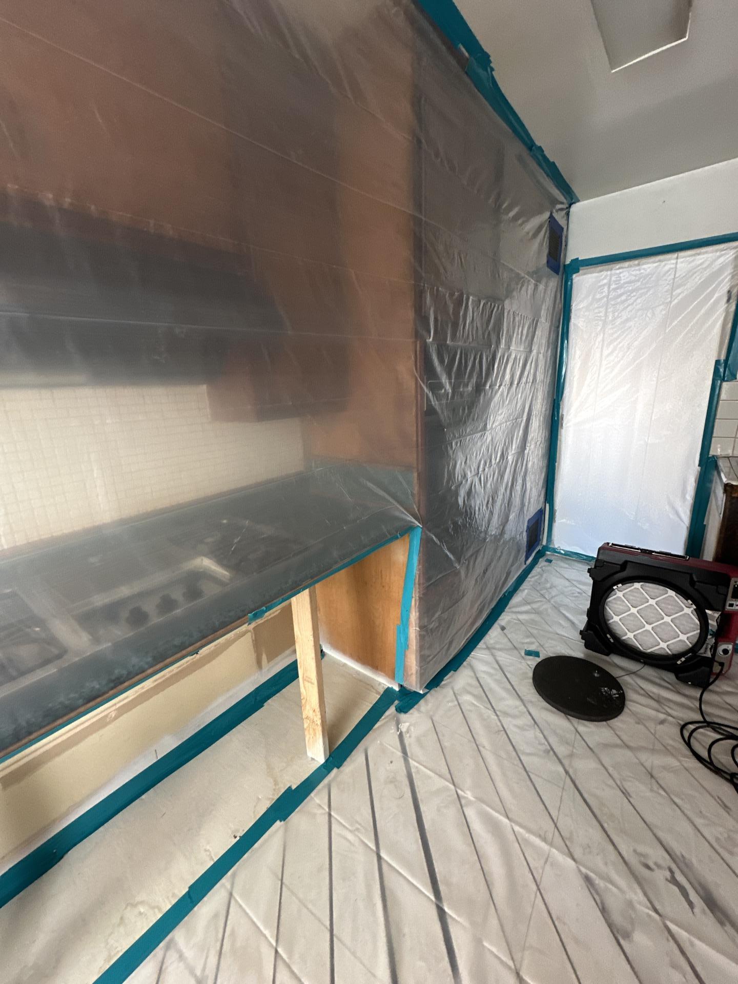 Emergency water mitigation showing kitchen cabinets and counters sealed within a containment zone with an air mover, ensuring aggressive structural drying and effective water damage restoration to prevent mold growth.