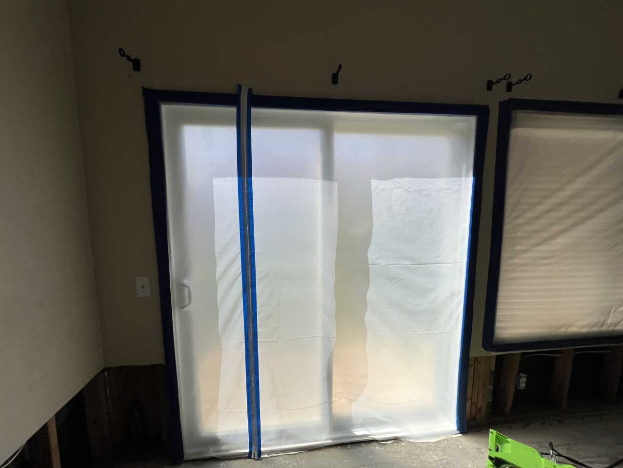 Water mitigation in progress showing plastic containment barriers over the window and slider to control air movement and facilitate efficient structural drying after water damage to the walls.