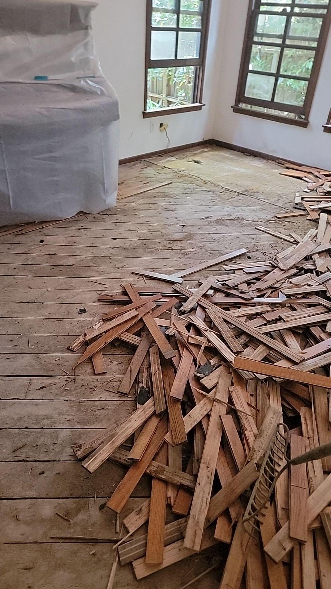 Emergency fire damage mitigation in the dining room showing damaged hardwood floor removal and debris removal to access the subfloor for smoke and soot cleanup and structural drying.