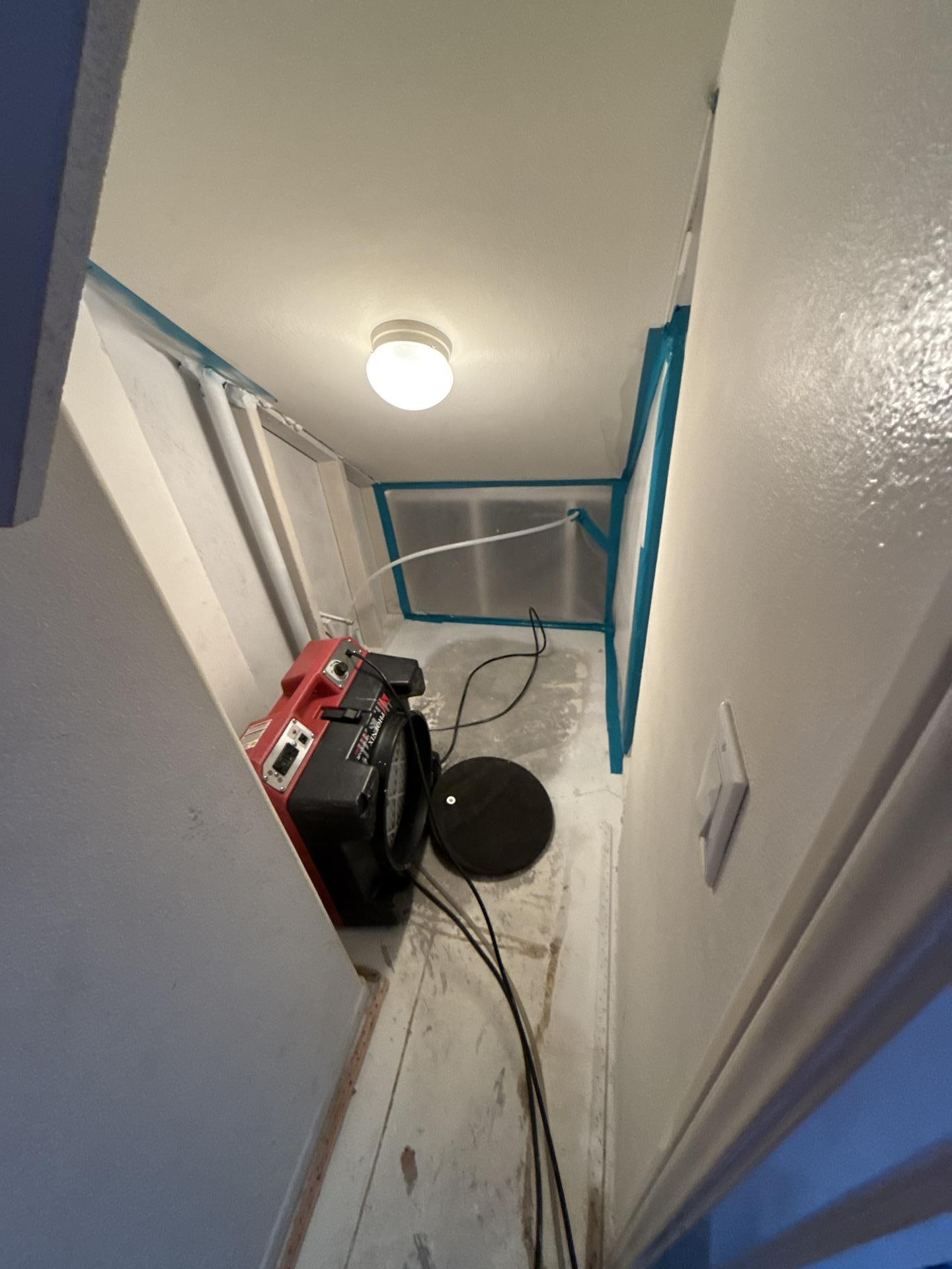 Water mitigation in a small hallway or closet showing professional air mover and drying setup within a sealed area to achieve effective structural drying and dehumidification after significant water intrusion.