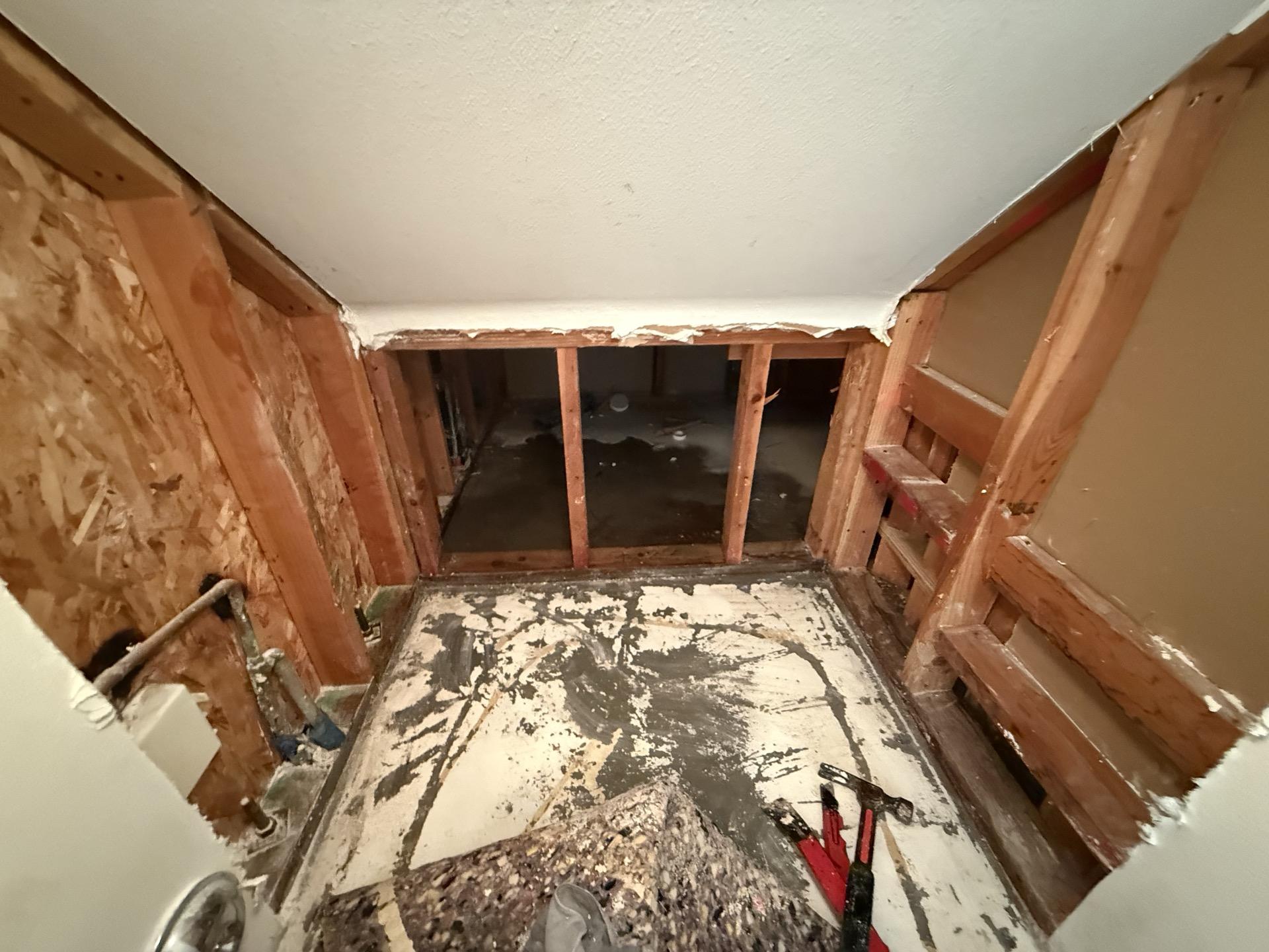 Water damage mitigation in progress showing removed drywall, exposed studs, and damaged subfloor, necessary for complete structural drying and mold prevention after significant water intrusion into the property.