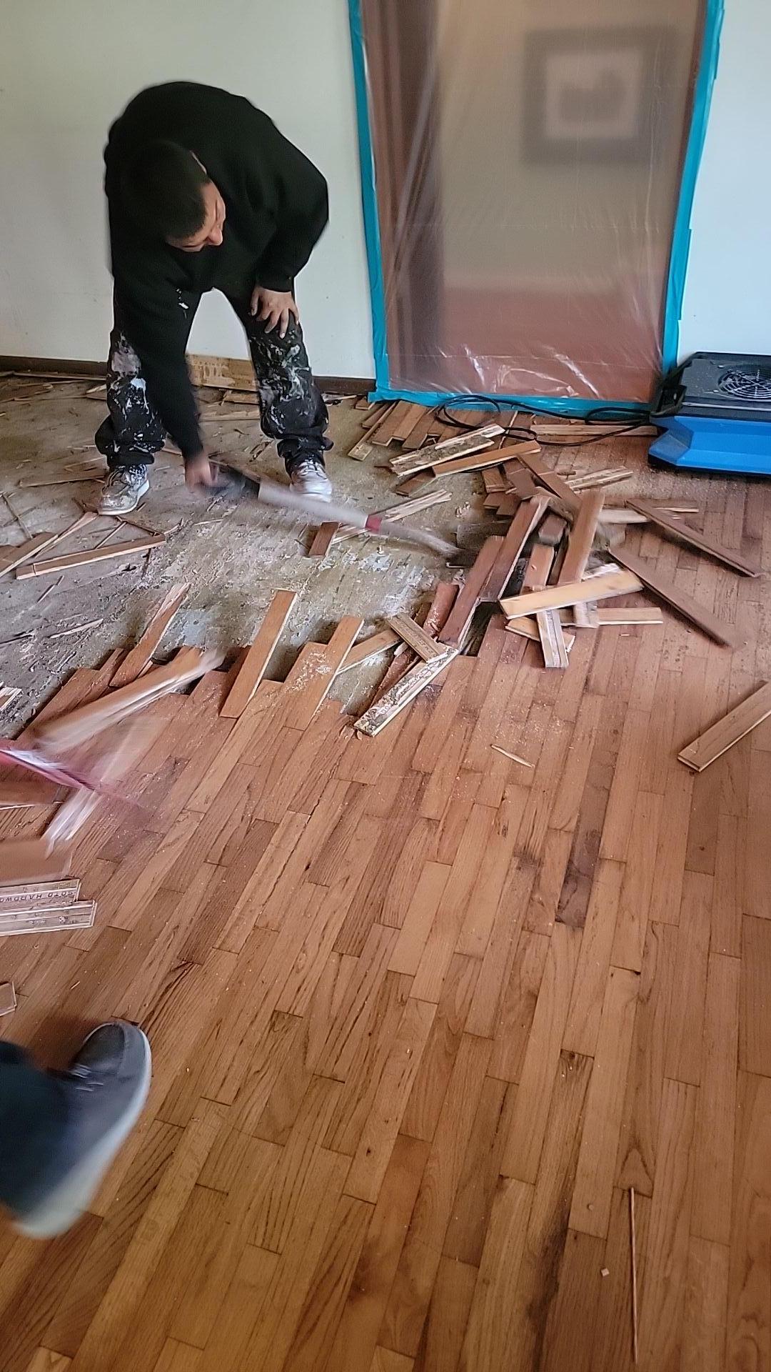 Technician performing demolition and removal of fire-damaged hardwood flooring in the dining room as part of emergency fire damage mitigation and initial soot cleanup preparation.