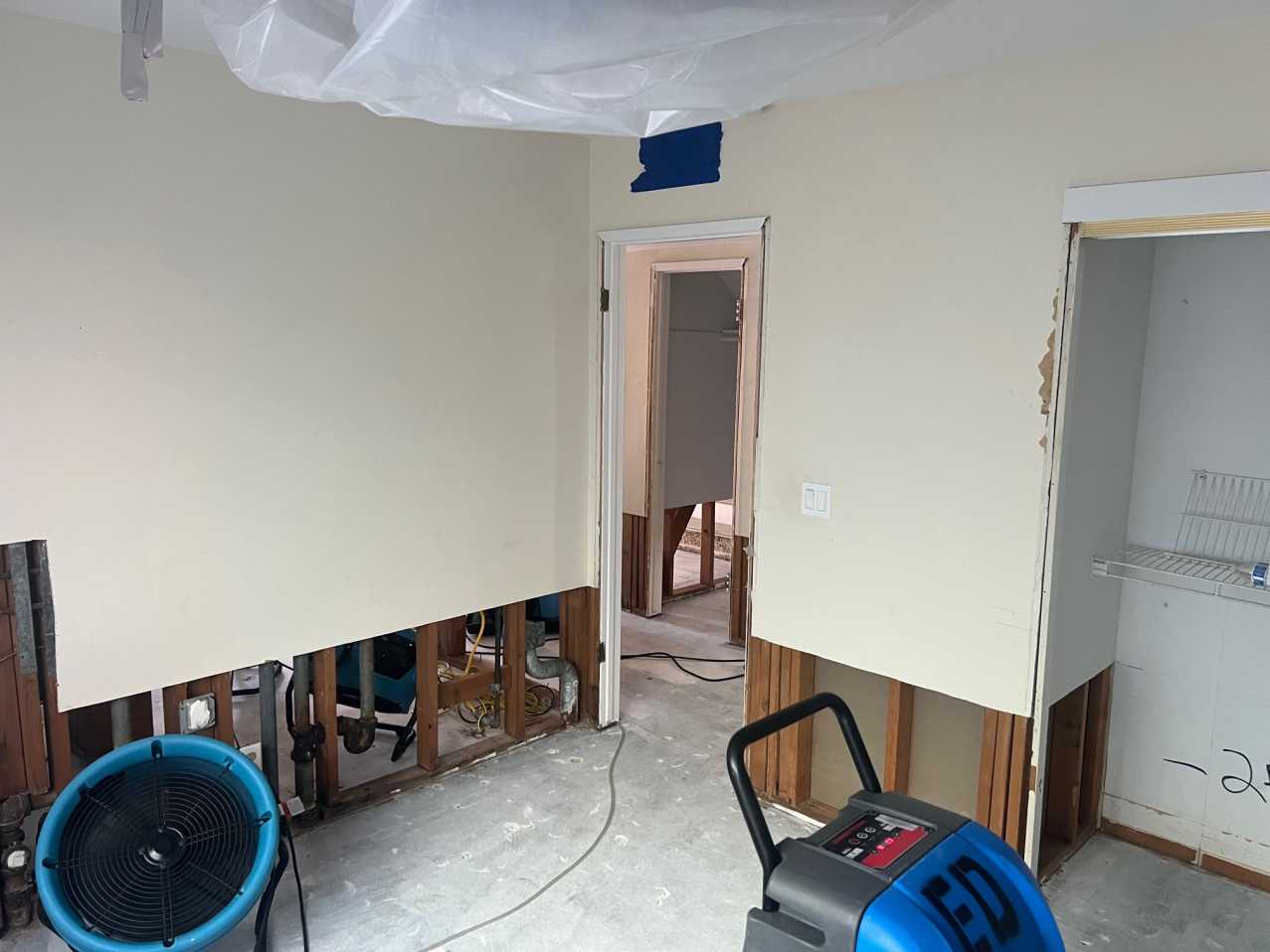 Reconstruction preparation showing removed drywall base, exposed studs, and drying equipment for final structural drying, a necessary step before property restoration and installation of new vinyl plank flooring and trim.