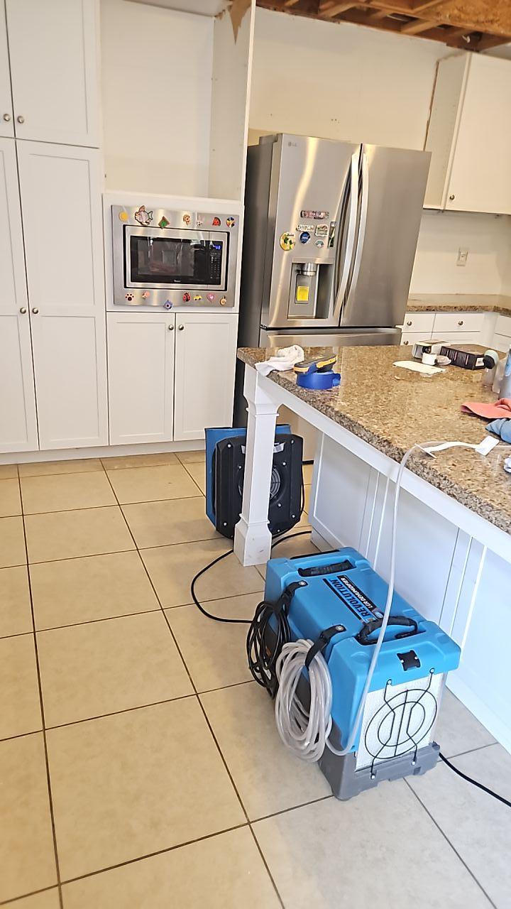 Water mitigation in progress showing professional air movers and dehumidifiers set up in a kitchen for structural drying and water extraction, critical steps in kitchen restoration after a plumbing leak.