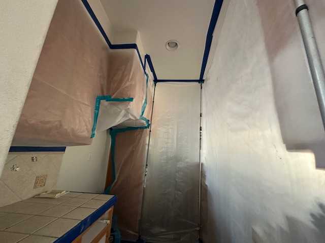 Water mitigation in progress showing a containment barrier setup in a kitchen area with plastic sealing off cabinets and doorways for focused structural drying and mold prevention after water intrusion affected the walls.